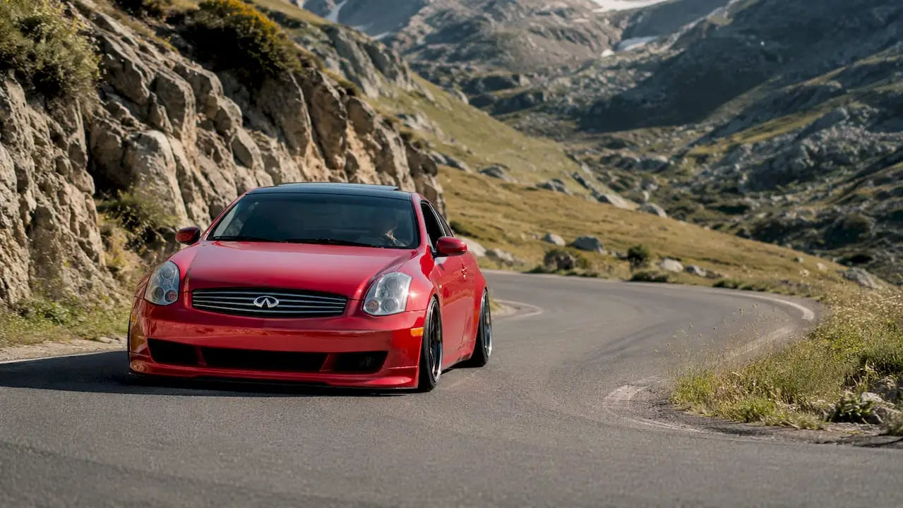 Red G35 car cornering on mountain road